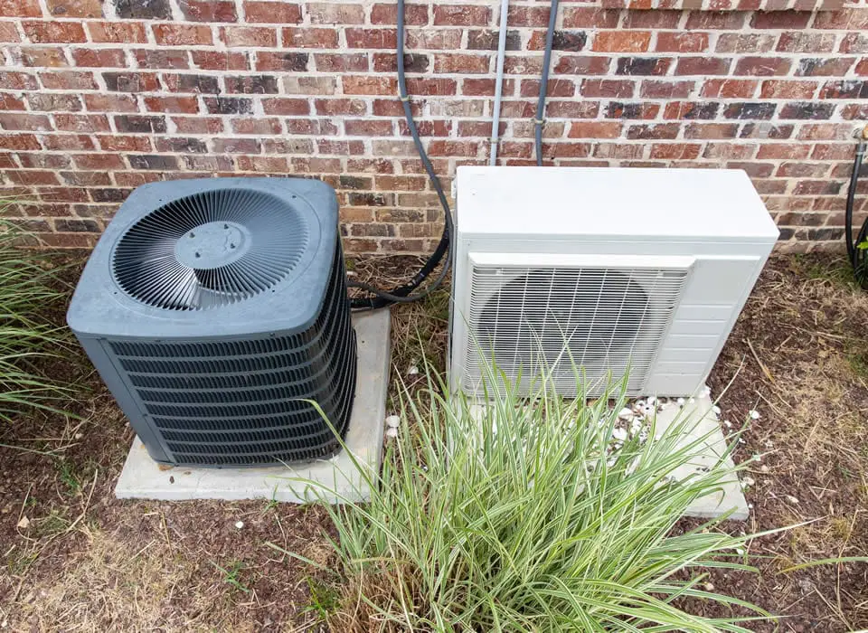 Comparison diagram showing a ducted heat pump system using a central air handler versus a ductless system using individual wall-mounted room units.