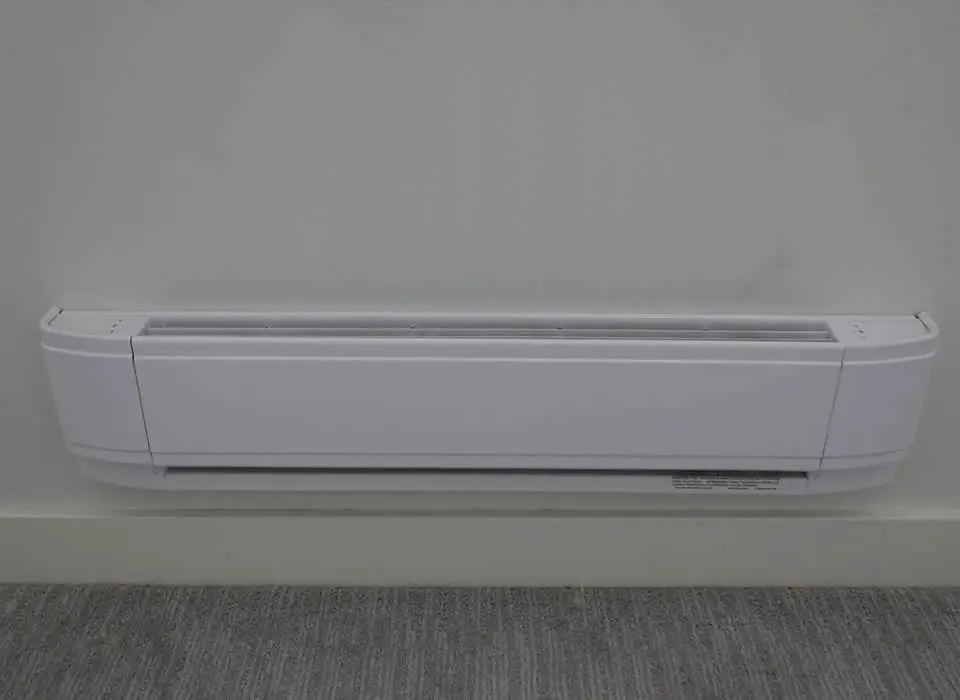 A sleek, white electric baseboard heater installed along the floor of a modern living room under a window to prevent cold drafts.